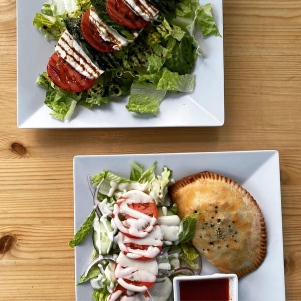 Two plates of salads, one with Caprese and the other with an empanada and ranch dressing.