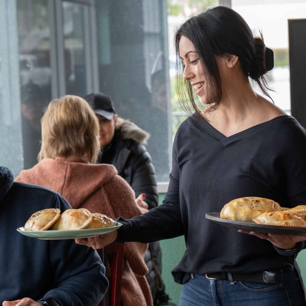 Smiling server handing plates of golden-brown Best Artisan Empanadas to customers in a restaurant.