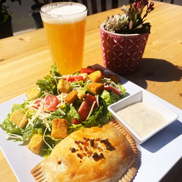 Best Artisan Empanadas meal with a golden-brown empanada, side salad, dipping sauce, and beer.